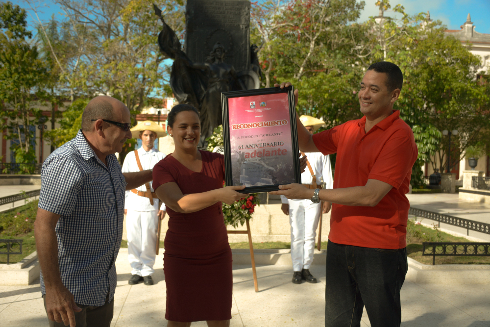 Jorge Enrique Sutil Sarabia, miembro del Buró Provincial del Partido y Raúl Hernández, funcionario de la Asamblea Provincial del Poder Popular entregaron el reconocimiento por los 61 años del rotativo camagüeyano a su directora Daicar Saladrigas González.Fotos: Alejandro Rodríguez Leiva/ Adelante